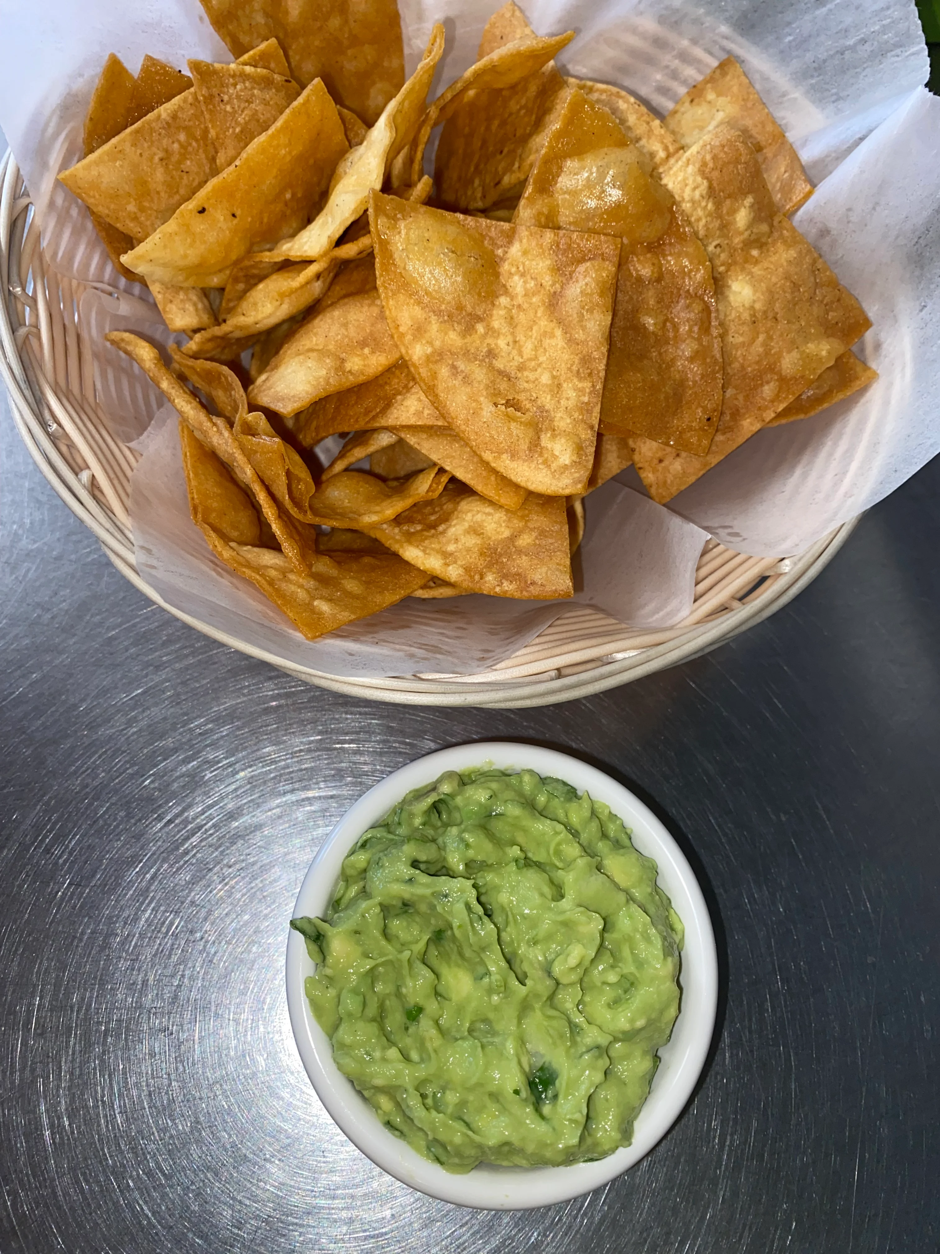 A basket filled with crispy tortilla chips accompanying a bowl of creamy guacamole.