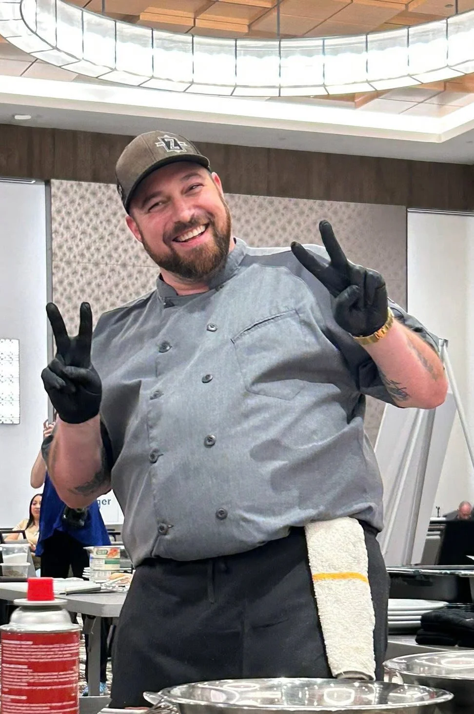 Chef smiling and posing with peace signs in a kitchen setting