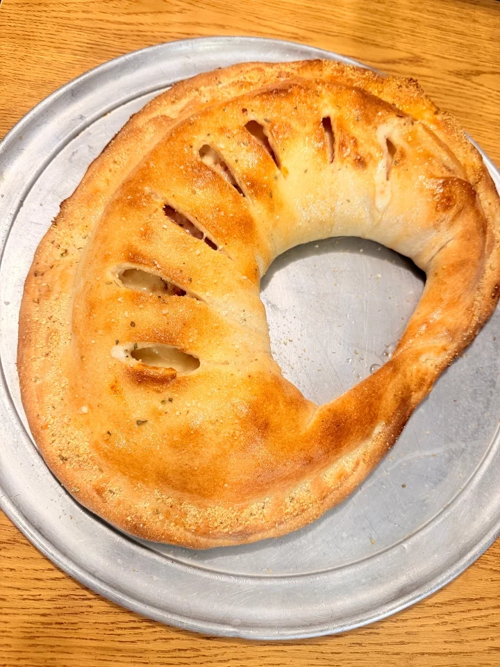 A golden-brown calzone with slits on top, presented on a round metal tray.