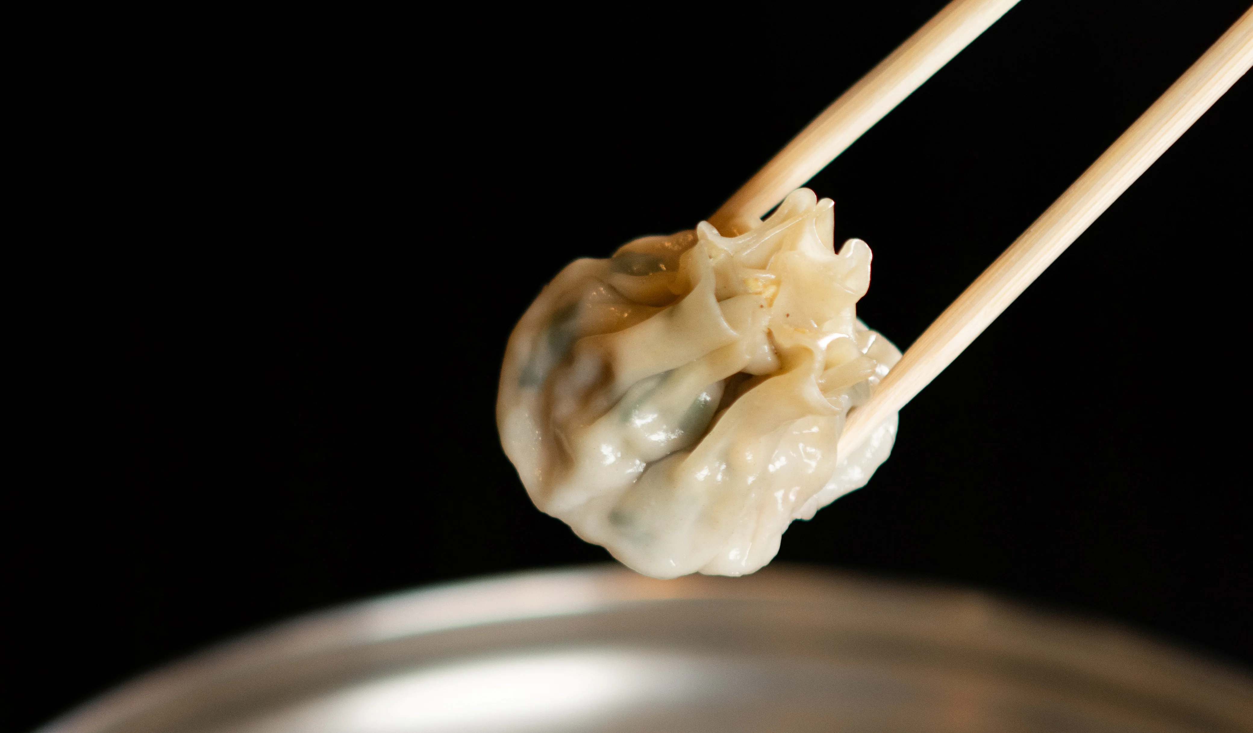 Steamed dumplings in a bamboo steamer, held with chopsticks.
