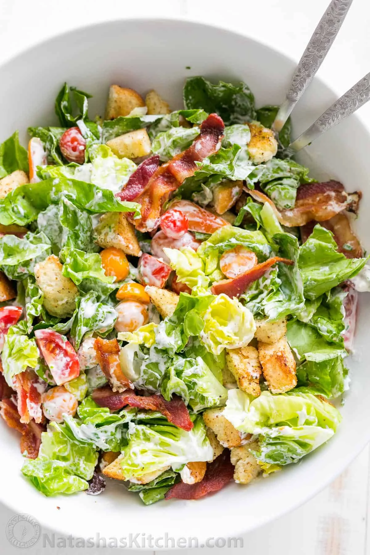 A fresh salad featuring mixed greens, tomatoes, croutons, and bacon, dressed in creamy dressing.
