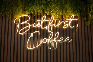 Neon sign reading 'But first, Coffee' in a cozy cafe setting