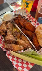 A platter of chicken wings featuring both saucy and dry-rubbed varieties. The wings are served with a side of ranch dressing and accompanied by celery sticks.