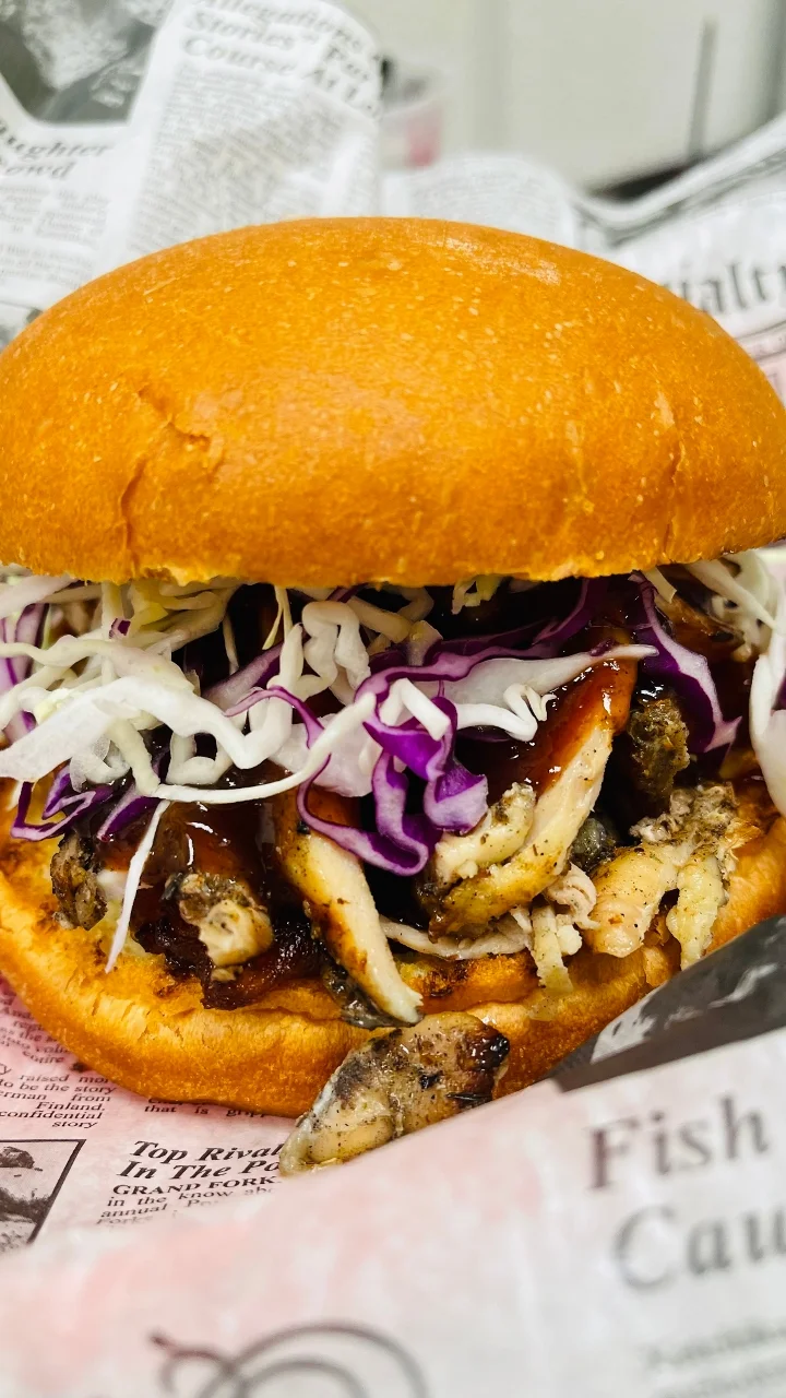 A delicious chicken sandwich featuring shredded chicken, coleslaw, and barbecue sauce, all nestled in a fluffy orange bun.