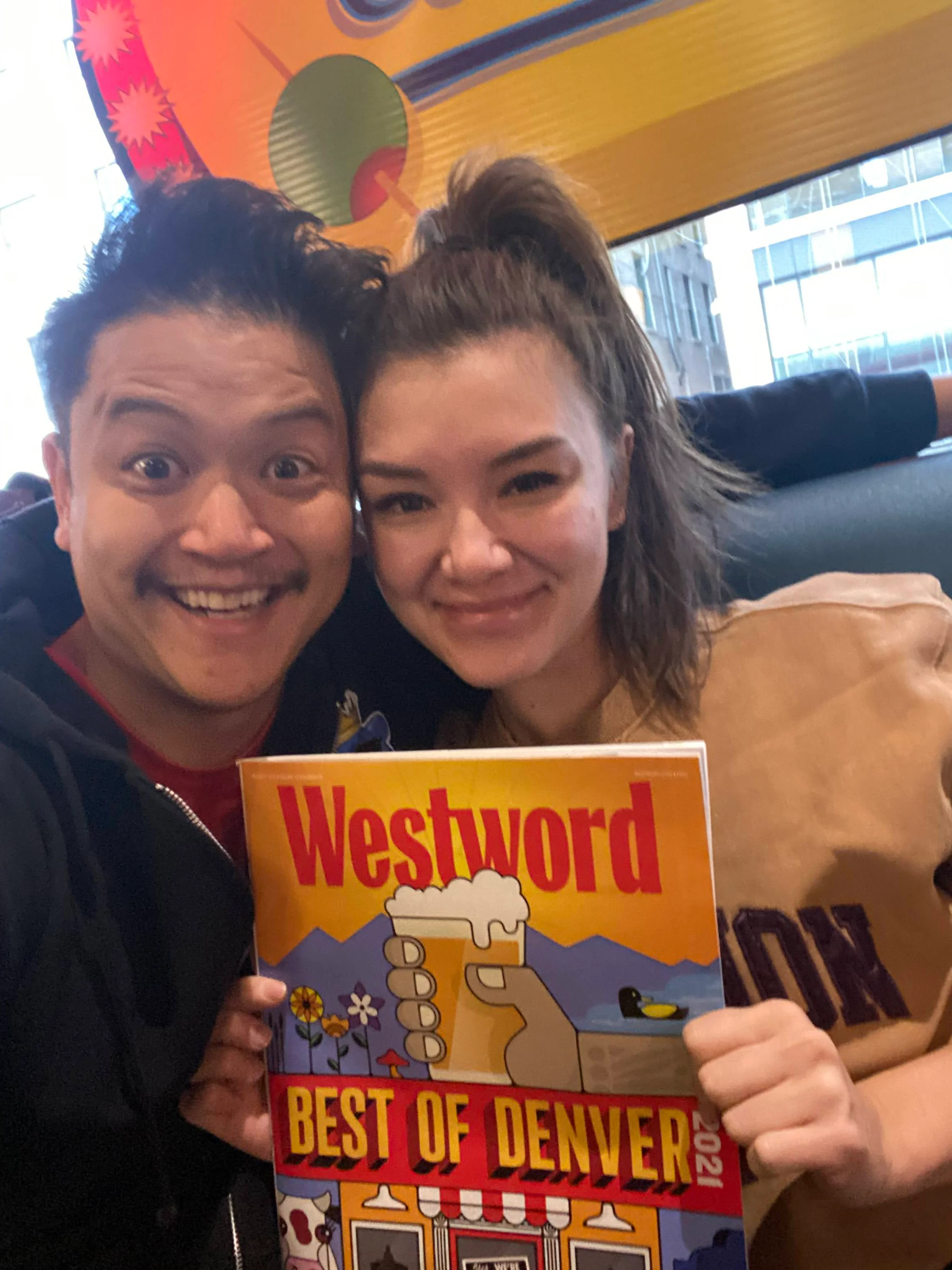 Two friends celebrating with a magazine in a vibrant restaurant setting