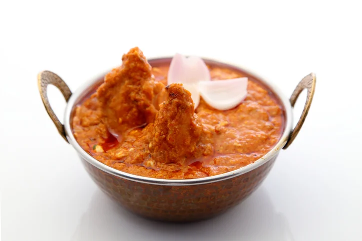 Indian butter chicken in a copper bowl with garnishes