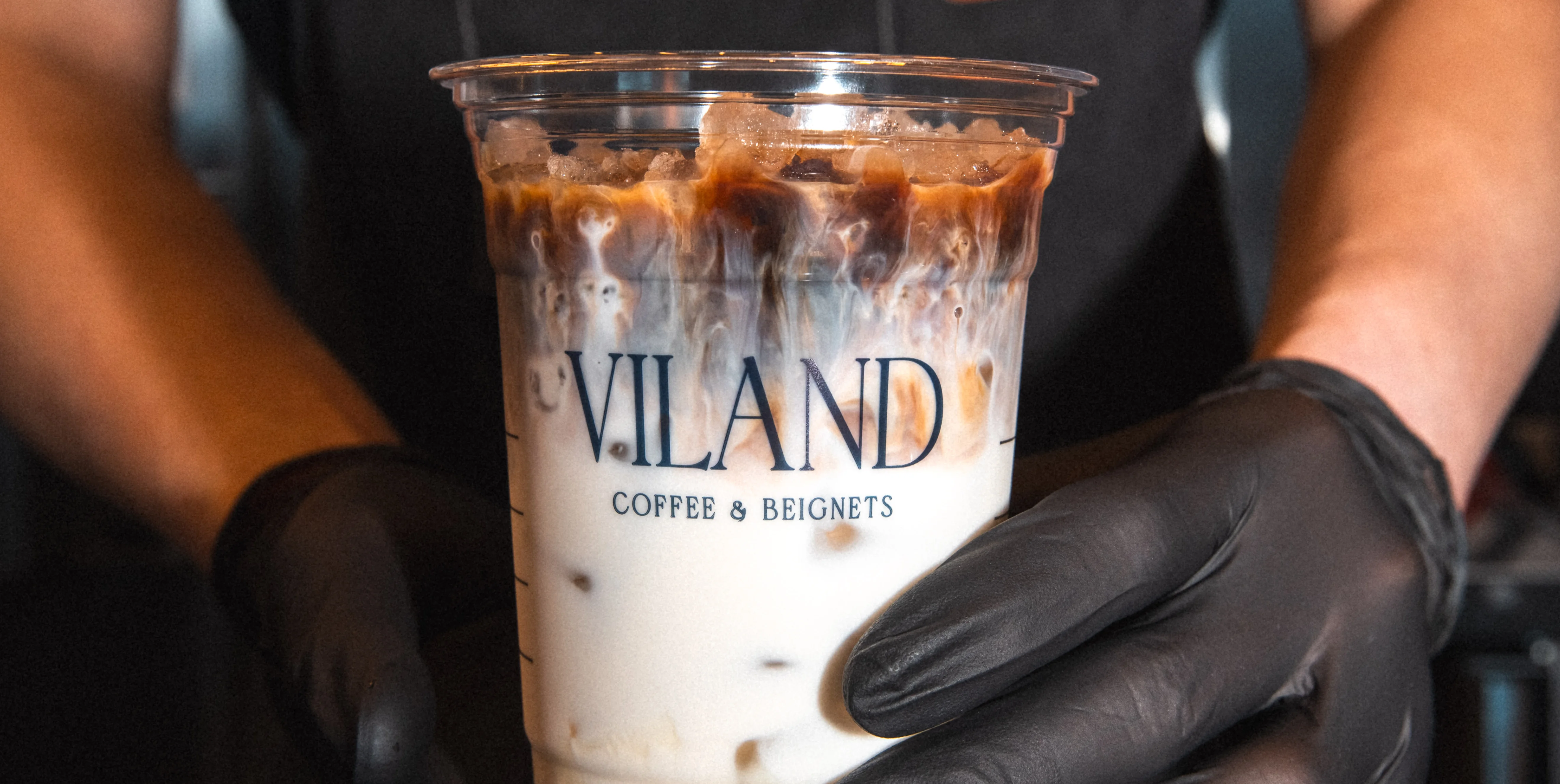 cup of iced coffee from ViLand coffee and beignets being held by two hands