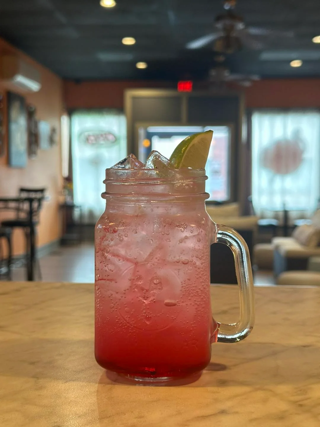 Refreshing pink cocktail with lime garnish in a cozy café setting