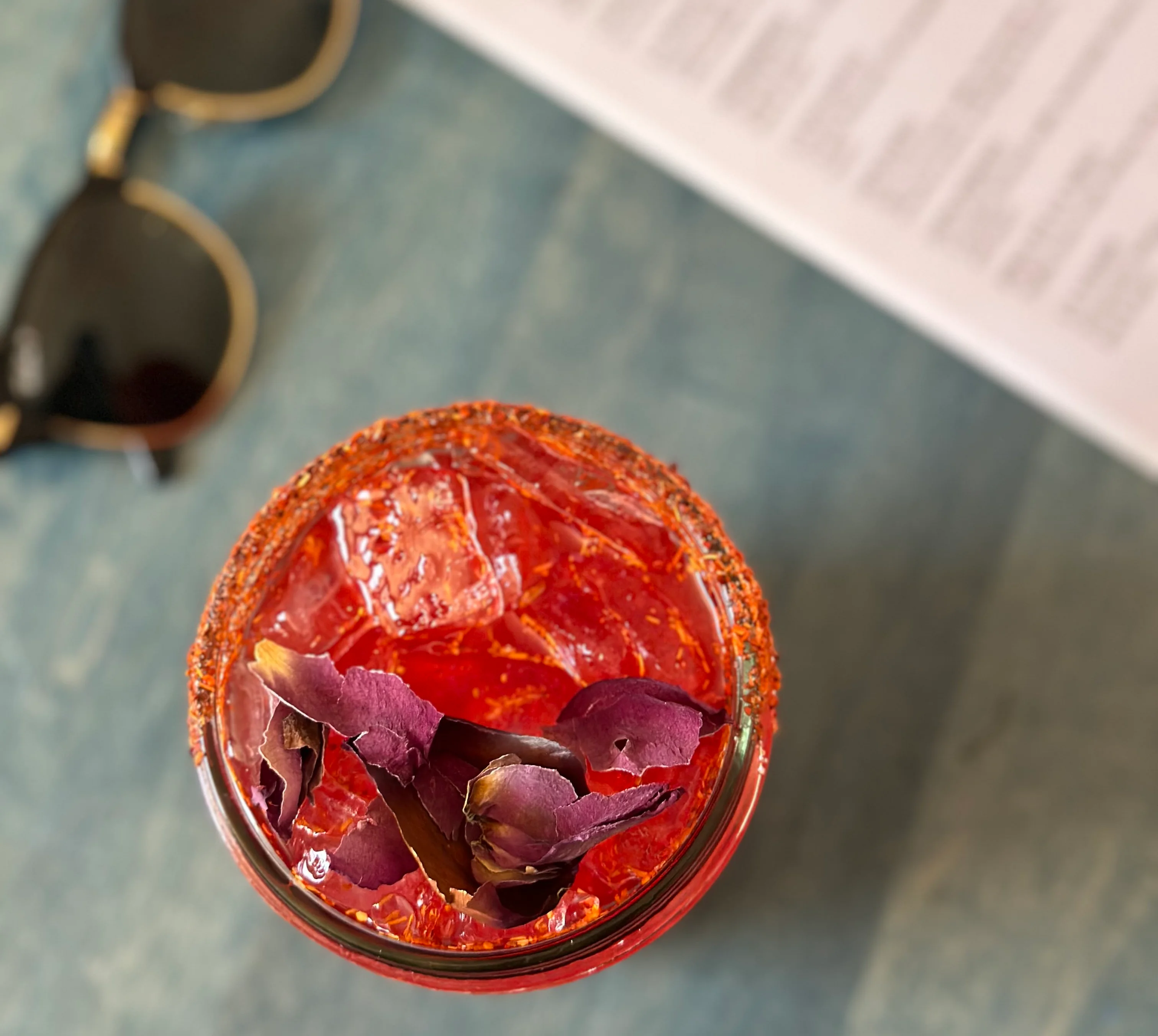 Vibrant cocktail garnished with rose petals and chili rim
