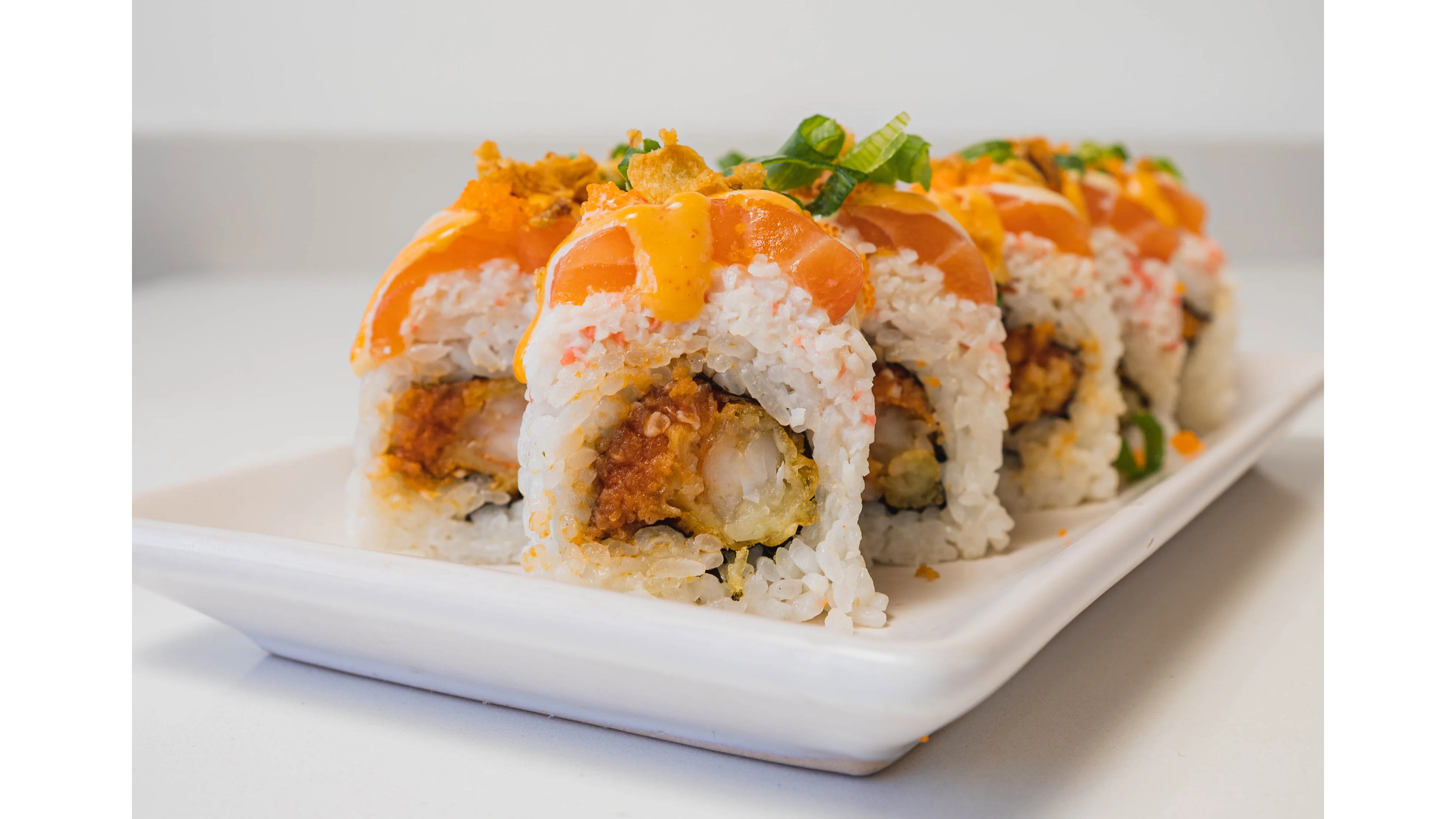 Delicious sushi rolls topped with salmon and spicy sauce on a white plate.
