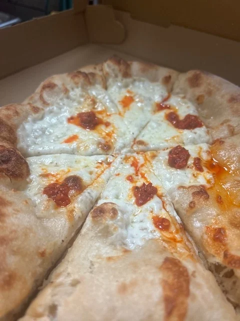 A close-up of a pizza with a thin crust, topped with cheese and bits of red sauce. The pizza is sliced into equal pieces.