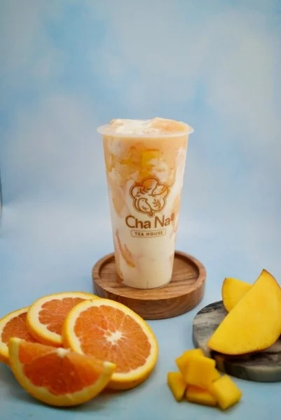 A fruity concoction featuring orange and mango, swirled together in a clear cup with a logo. Fresh orange slices and mango pieces are arranged around it for a vibrant presentation.
