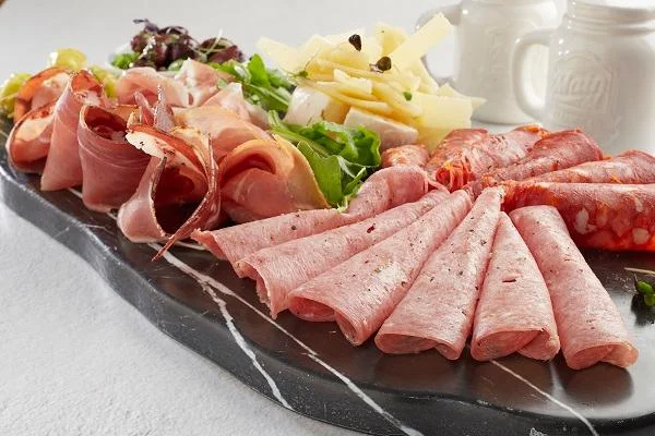 A charcuterie board displaying a variety of cured meats and cheeses, alongside leafy greens on a marble serving platter.