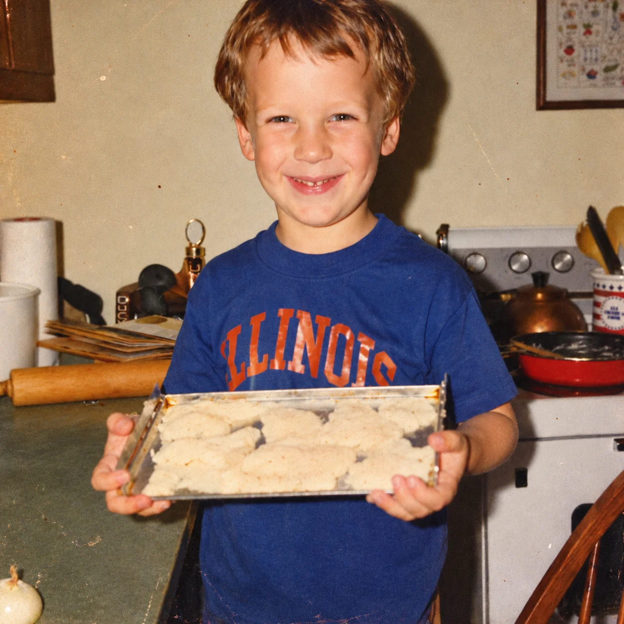 Child smiling in kitchen holding a tray of homemade cookies