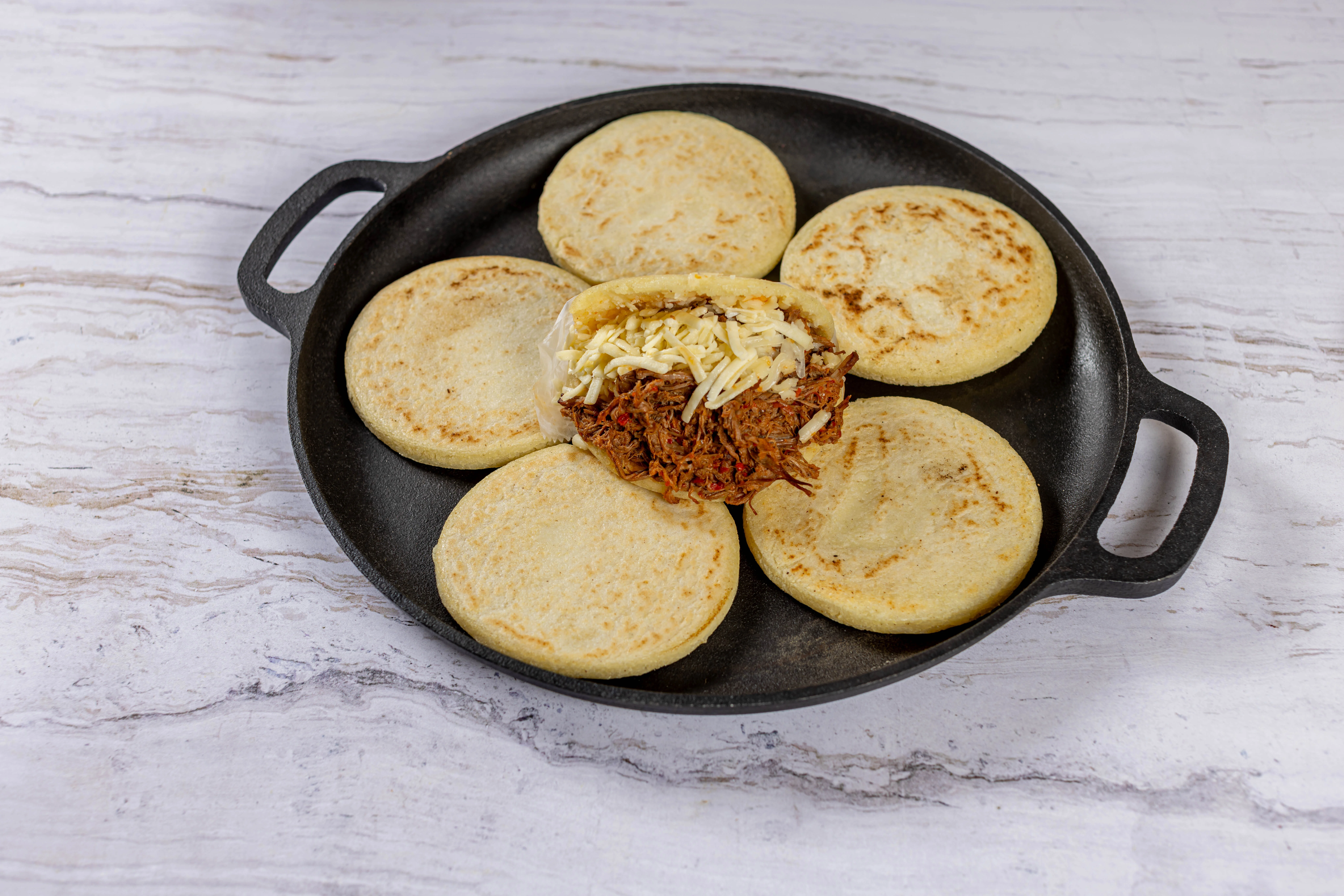 Freshly made arepas on a traditional budare (griddle), with one stuffed with juicy shredded beef and cheese at El Budare Cafe.