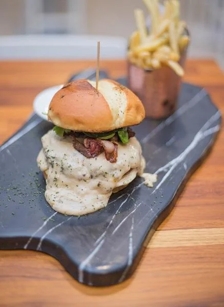 A decadent burger topped with gravy, served with a side of fries, placed on a stylish marble board.