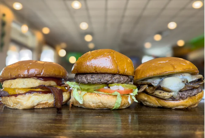 Three gourmet burgers on a wooden table in a casual dining setting