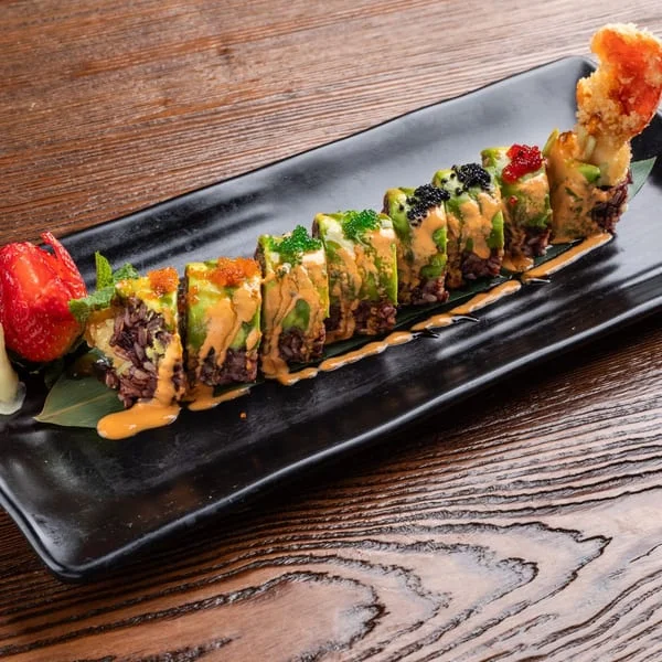 Colorful sushi roll with avocado and spicy sauce on a black plate