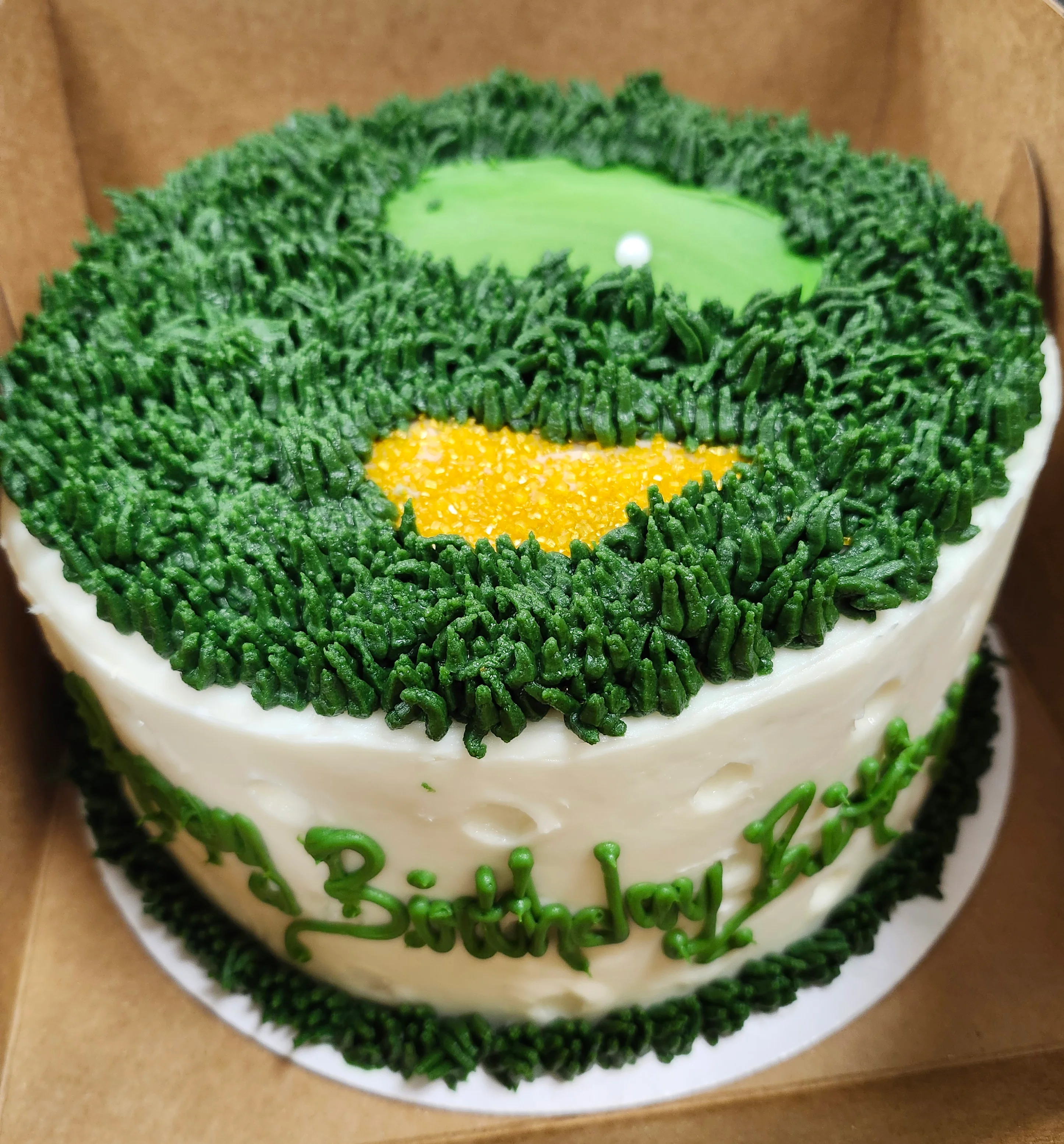 Round cake decorated to look like a golf ball on the sides and the top to look like a golf course.