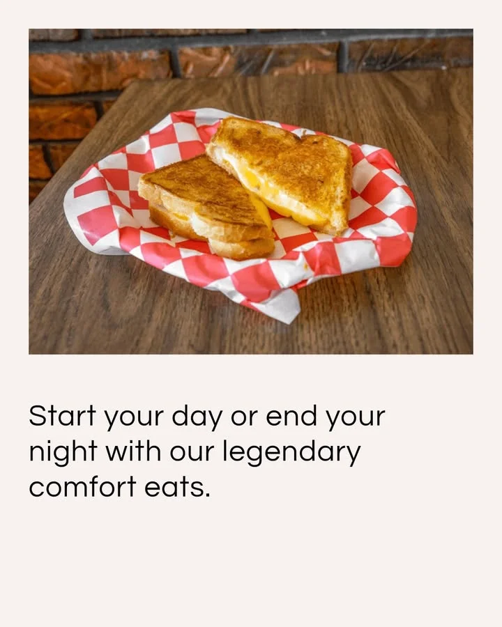 A cheeseburger featuring two patties, melted cheese, pickles, and mustard on a toasted bun, served on a checkered paper.