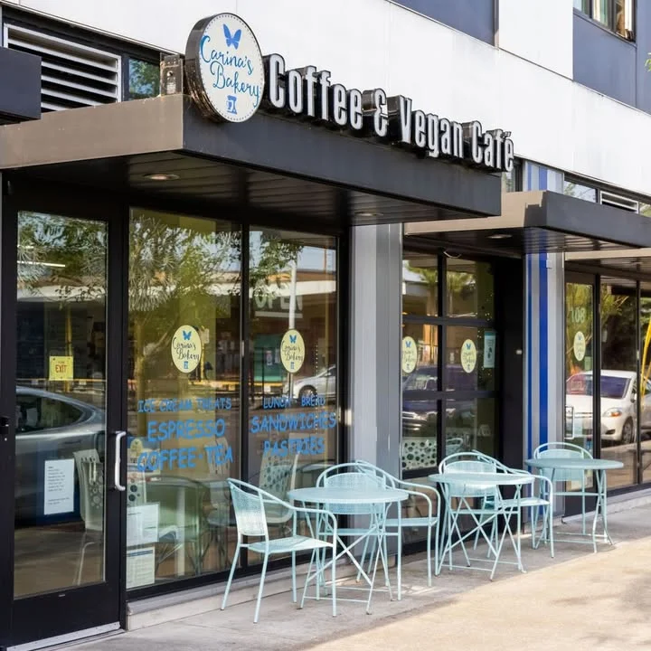 The exterior view of a coffee and vegan café featuring large glass windows and outdoor seating. The cafe's sign highlights its offerings.