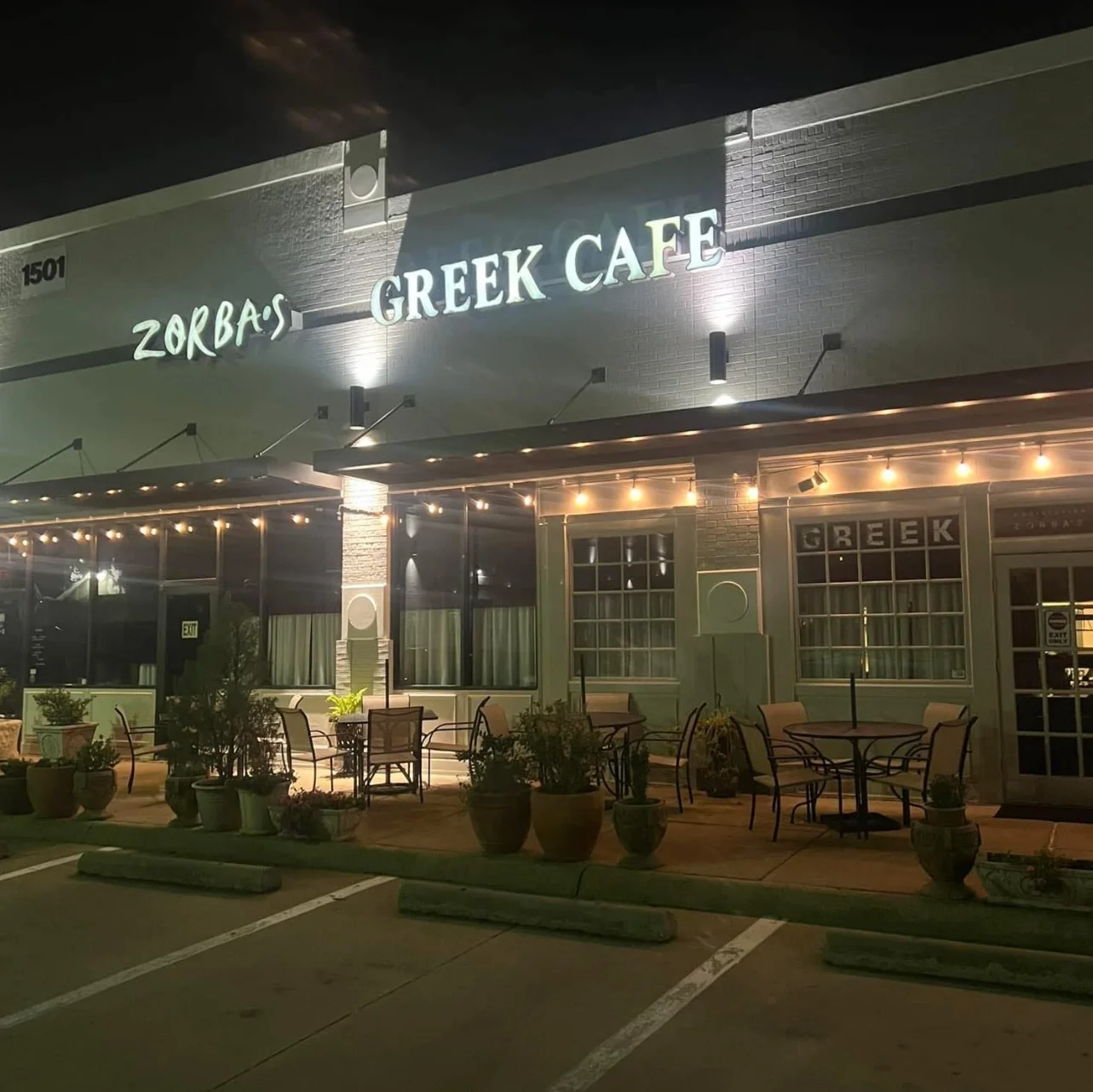 An exterior view of Zorba's Greek Cafe at night, illuminated with string lights and featuring outdoor seating.
