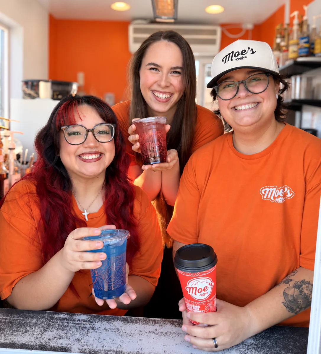 Smiling coffee shop staff holding iced drinks behind the cafe counter