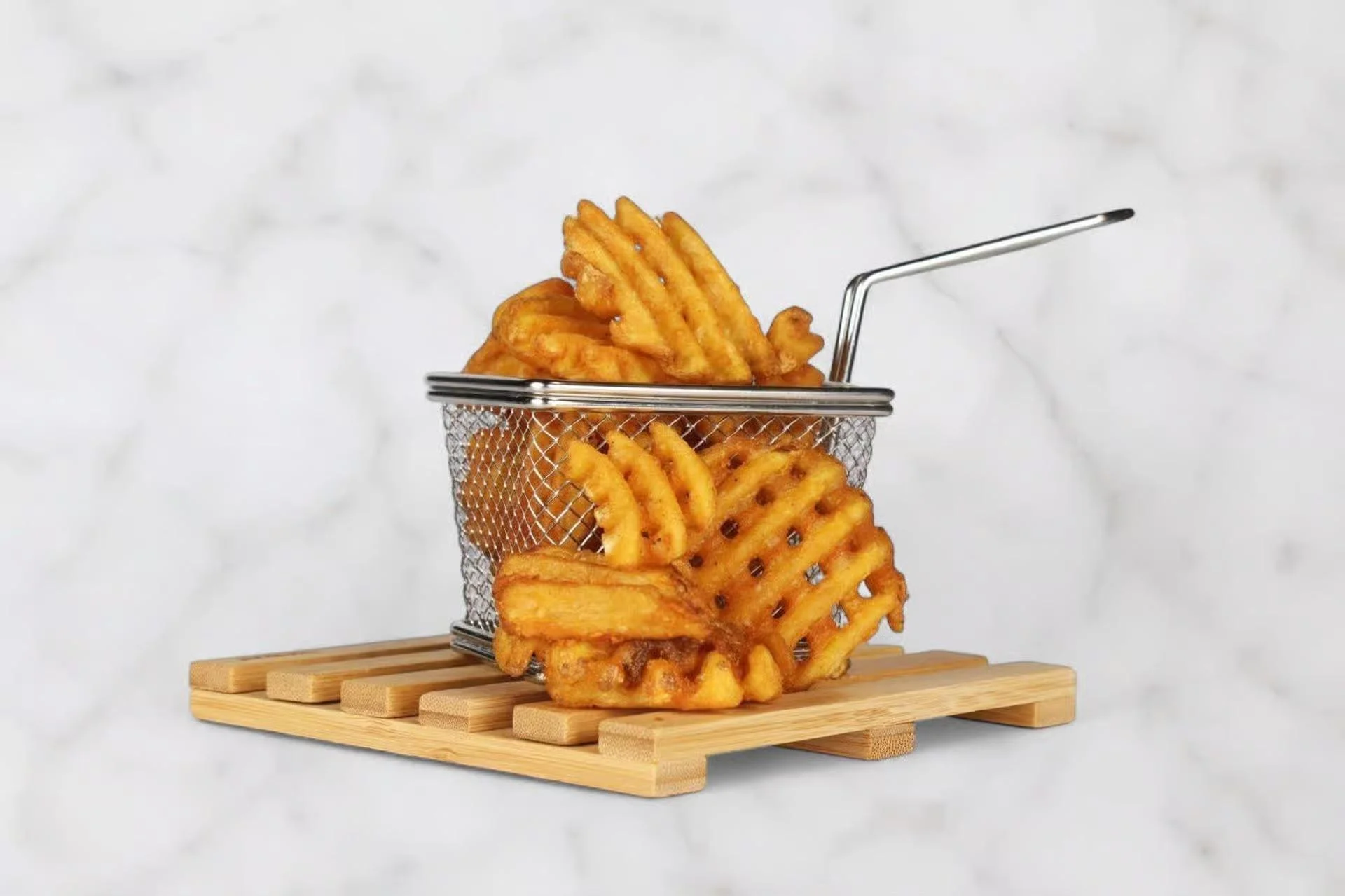 A serving of golden waffle fries in a metal basket on a wooden tray.