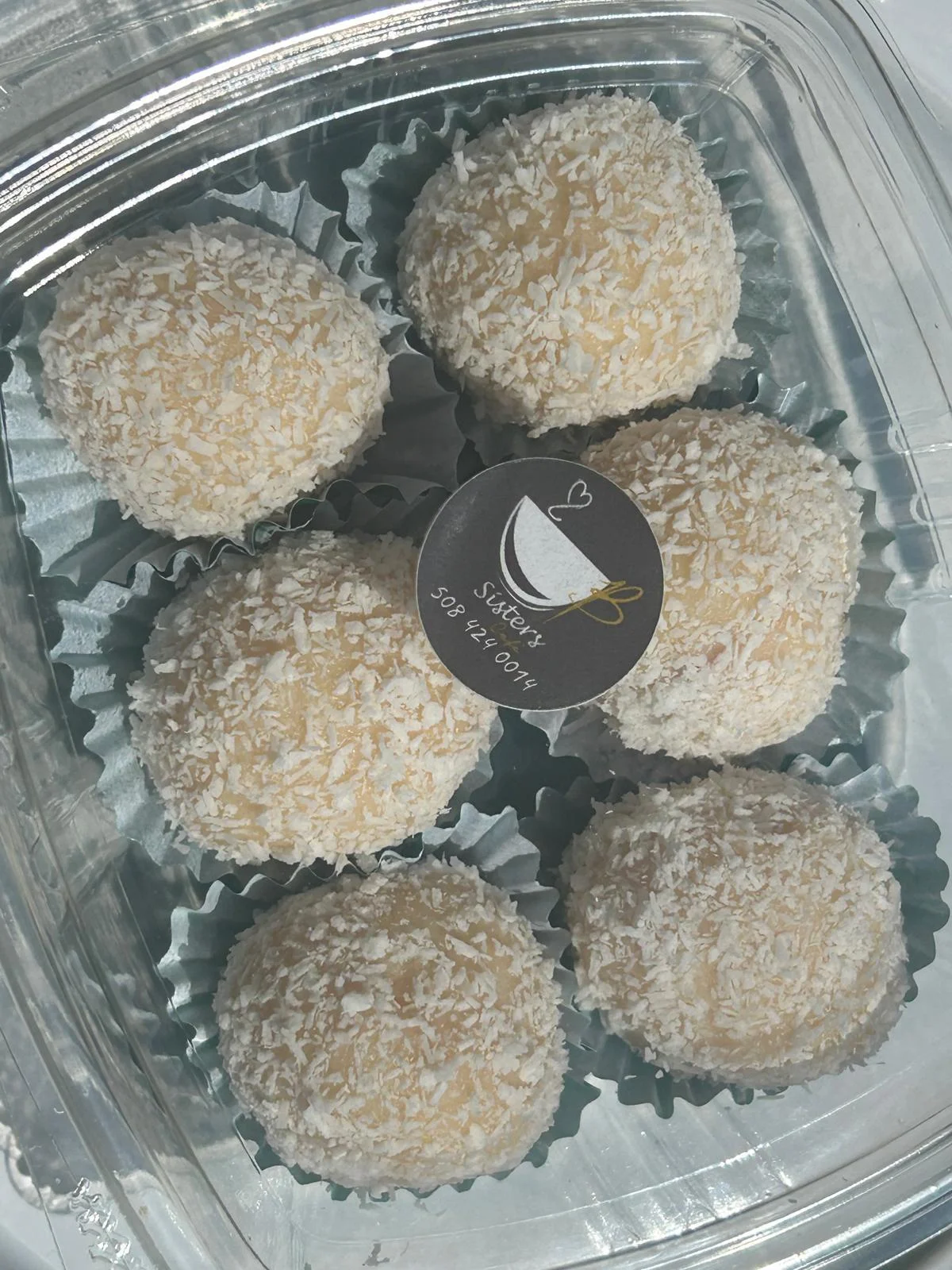 A clear container filled with round coconut-covered sweets, arranged neatly with a round label on top.
