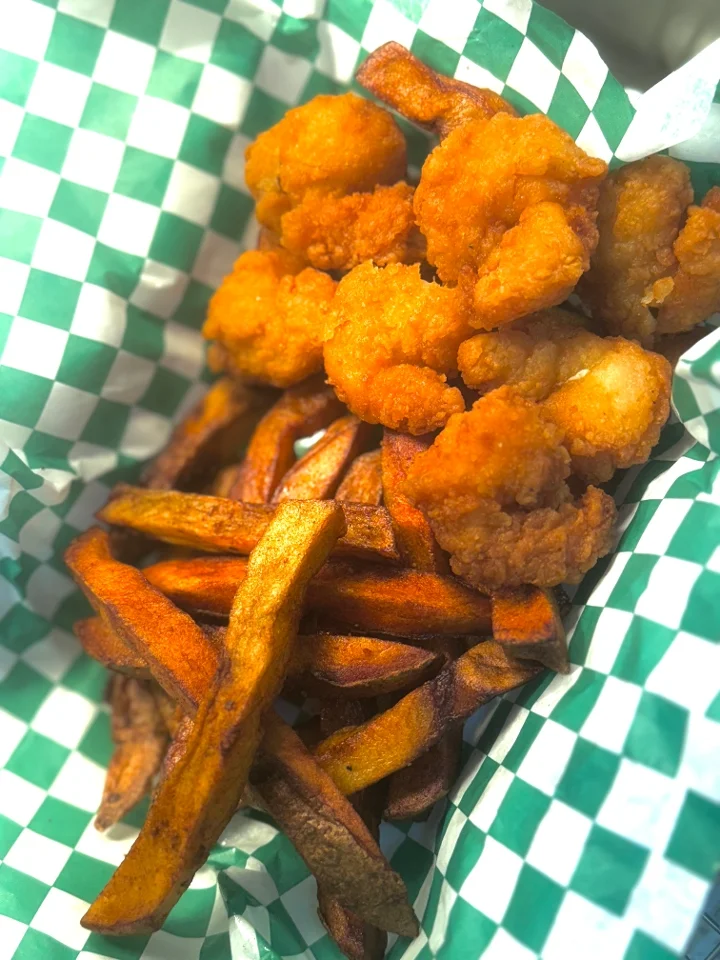 A combination of fried shrimp and sweet potato fries served in a basket with green and white checked paper.