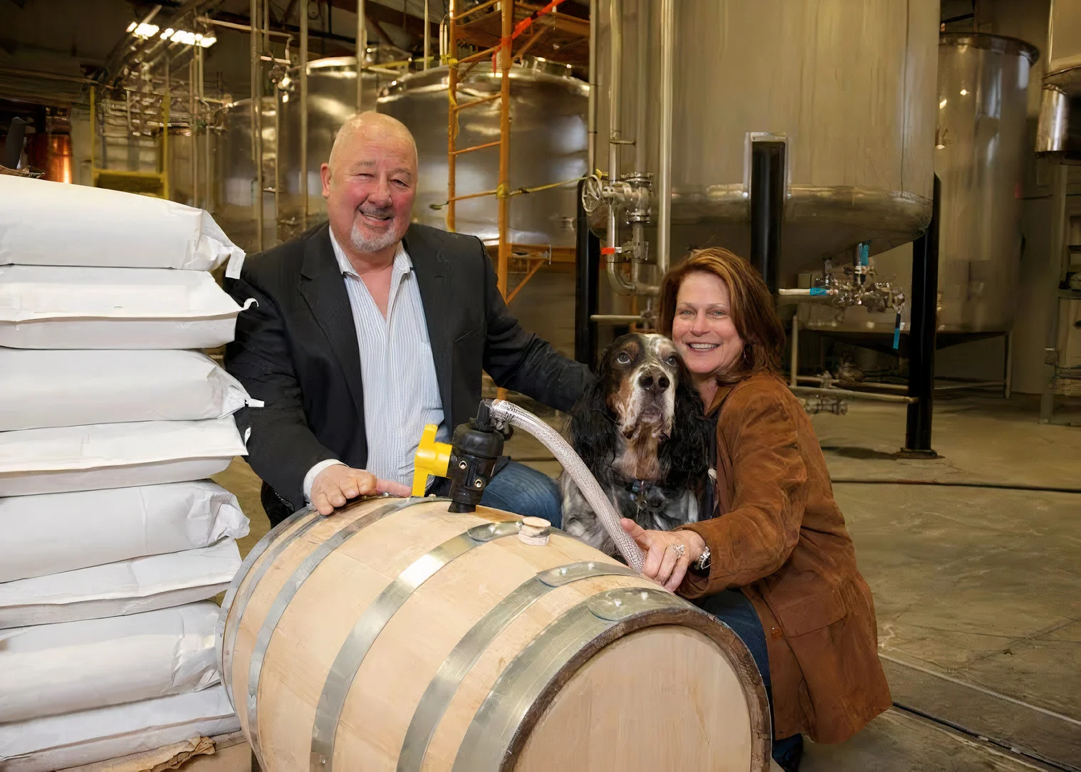 Brian & Reneé Bemis smile with a whiskey barrel and their dog in the distillery