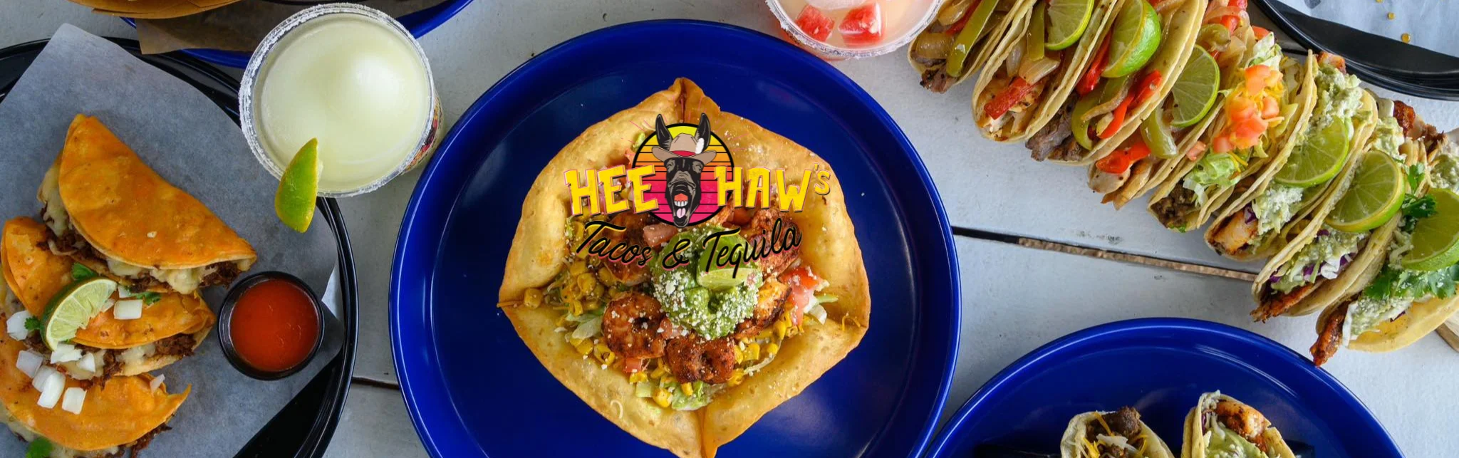 A colorful arrangement of tacos and a large taco salad with various toppings, set on a wooden table.