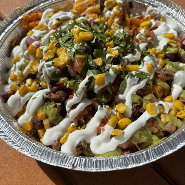 A vibrant platter of nachos topped with a mix of ingredients including corn, diced tomatoes, cilantro, and a drizzle of creamy sauce.