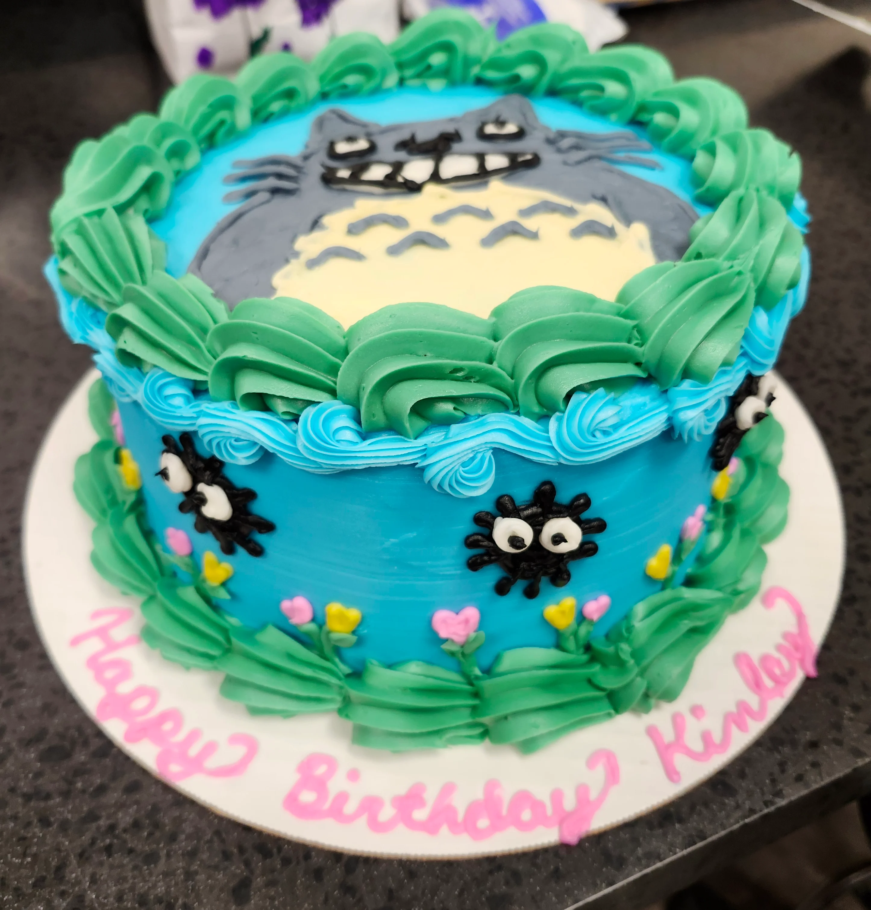 Round cake decorated with Studio Ghibli characters [soot sprites & Totoro] and the cake board says "Happy Birthday Kinley"