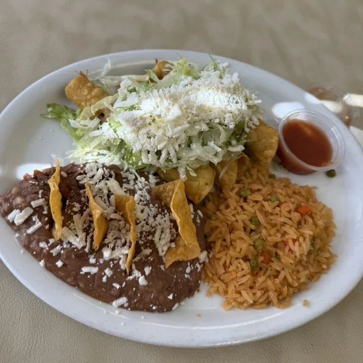 A plate of Mexican food featuring refried beans topped with cheese, a serving of rice, and a salad garnished with shredded lettuce, tortilla chips, and salsa.