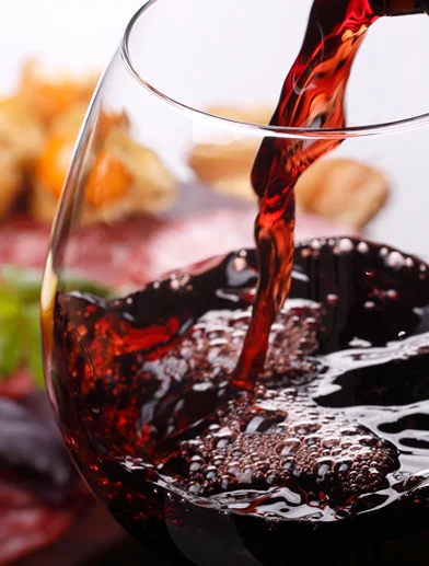 Pouring red wine into a glass with a charcuterie board in the background