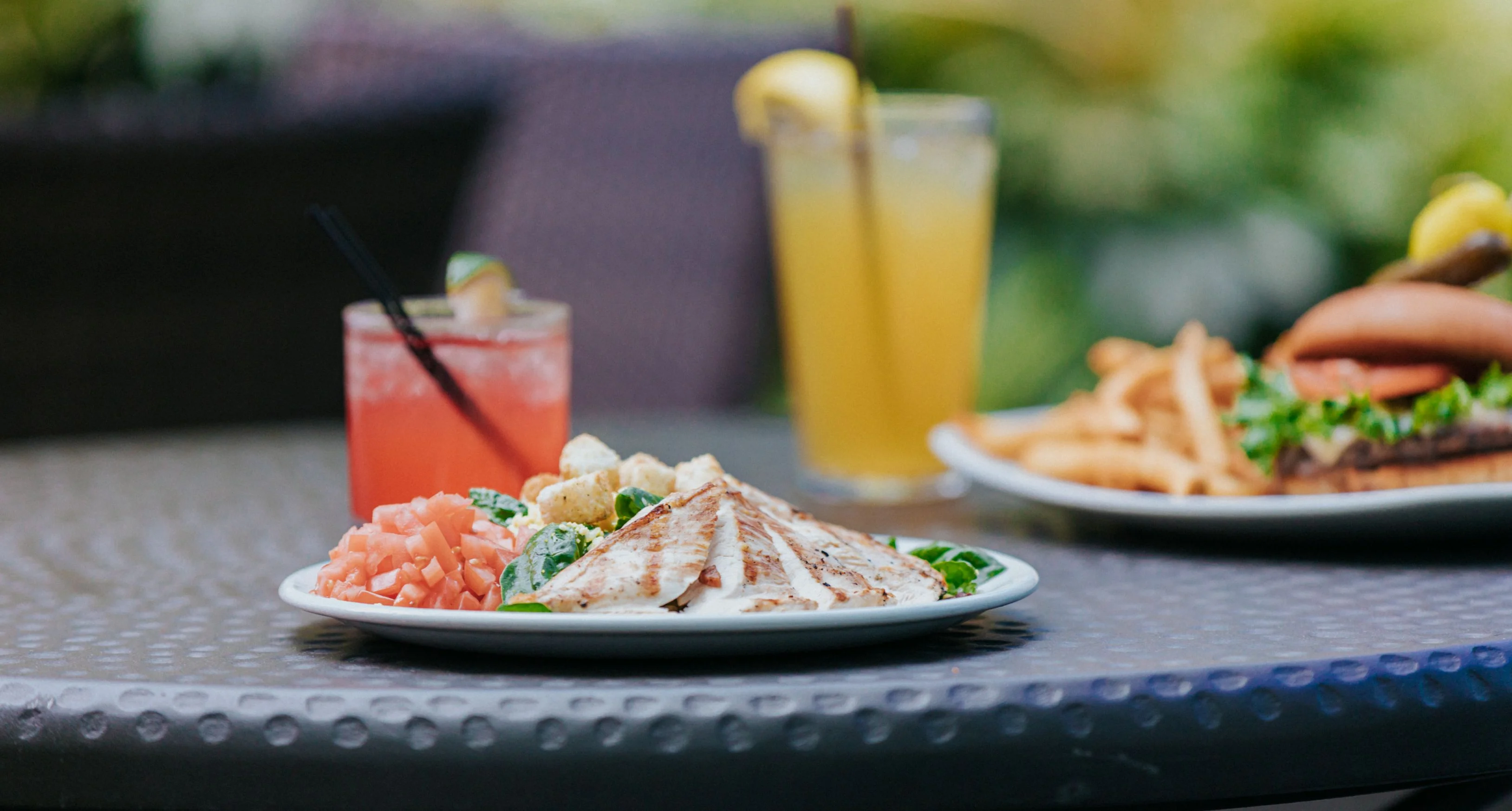 Grilled chicken salad with drinks on a table in a restaurant setting.