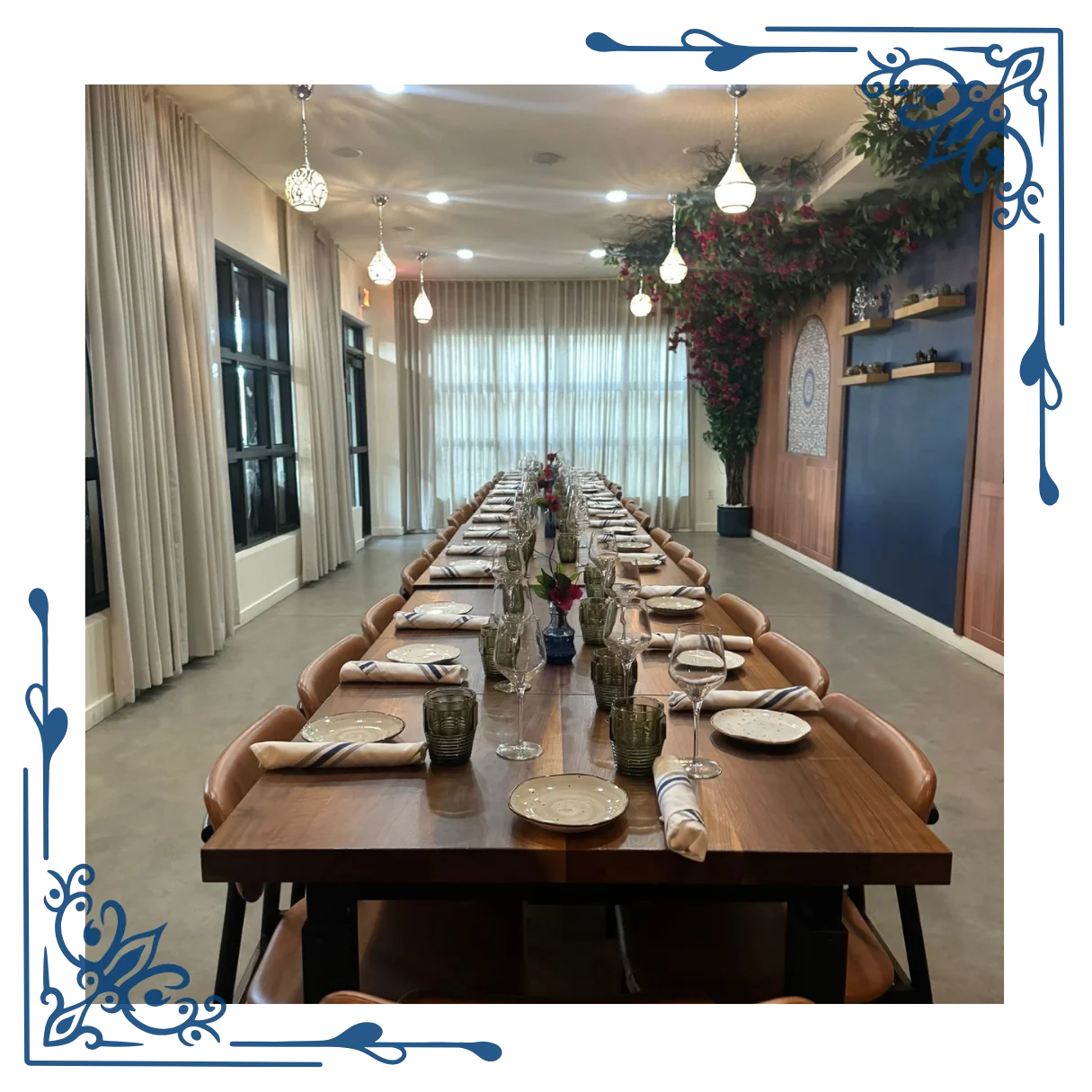 An image of sufrat private dining room, with dining plate sets, juice and wine glasses with napkins neatly arranged on a long brown wooden table with rows of brown wooden dining chairs on both the right and left side of it.