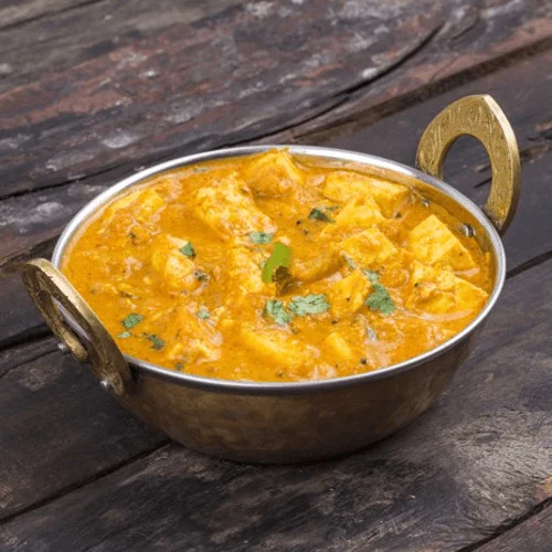  paneer butter masala in a traditional bronze serving bowl.