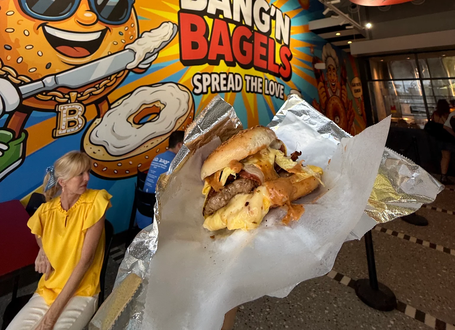 A delicious bagel sandwich in front of a colorful restaurant mural.