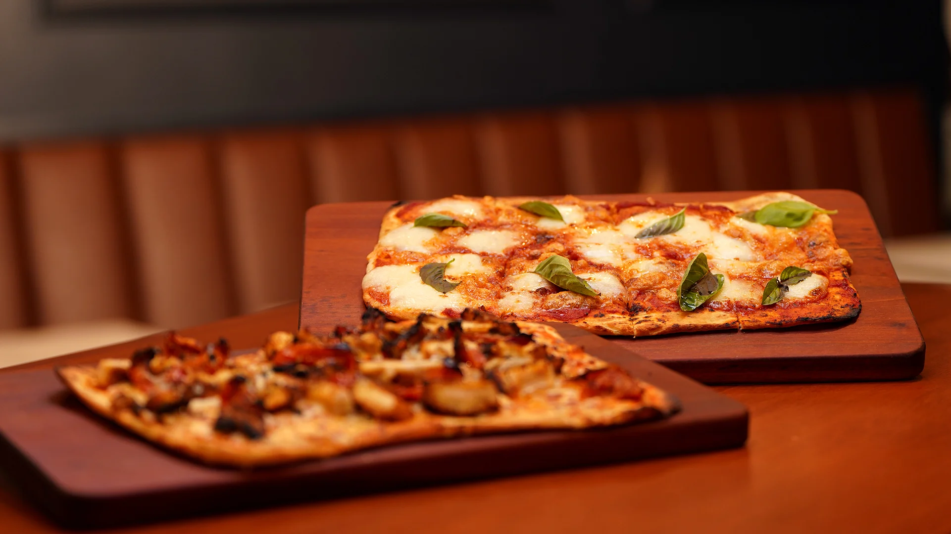 Two gourmet pizzas on wooden boards in a restaurant setting
