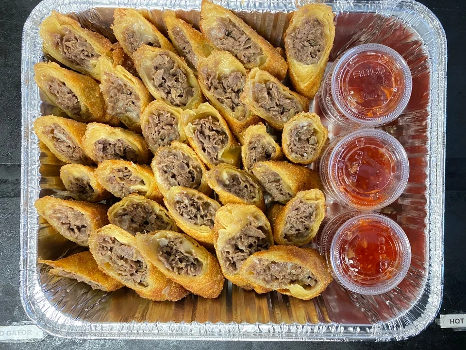 A tray filled with crispy beef-filled egg rolls, arranged neatly alongside three dipping sauces.