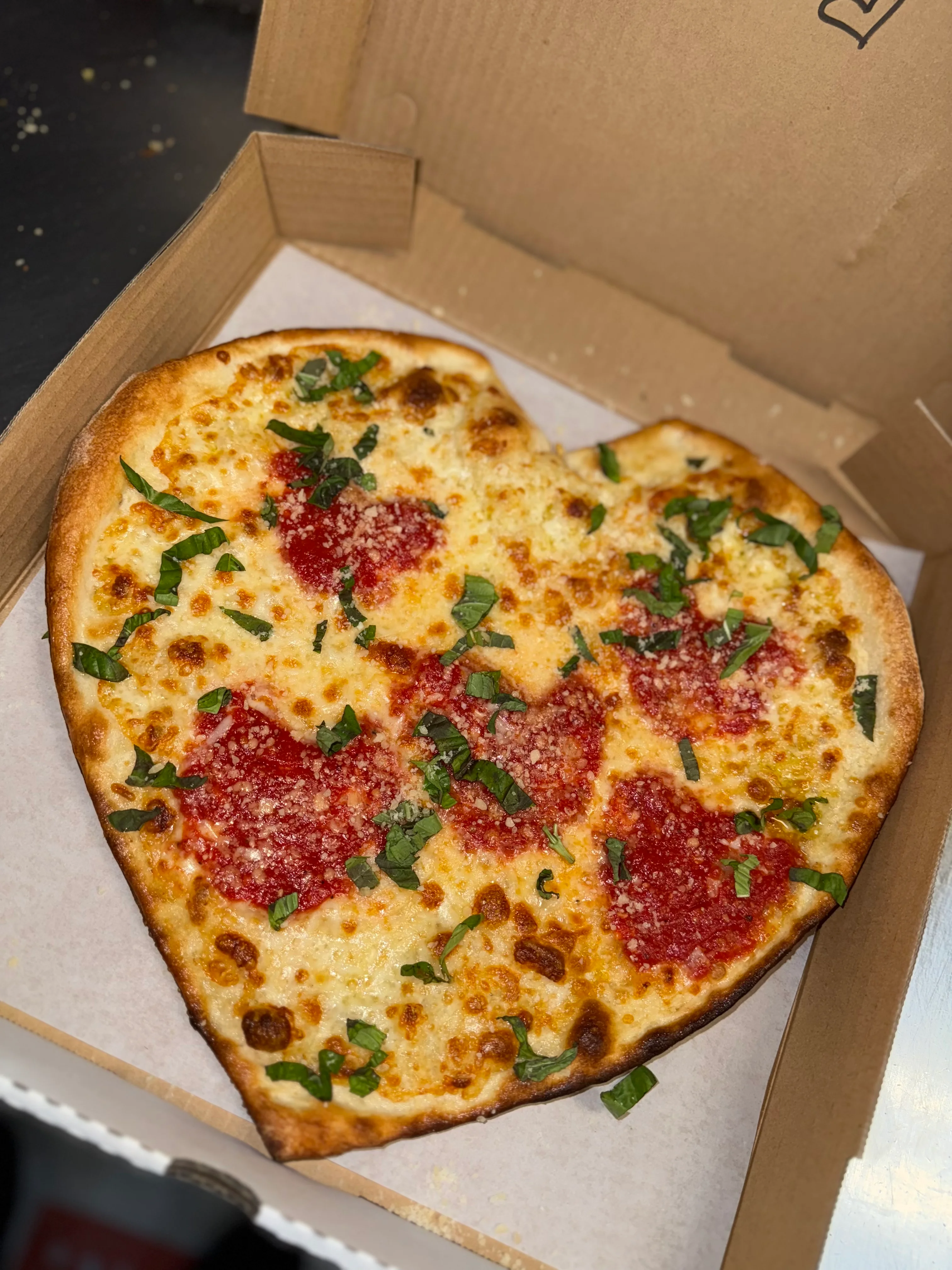 Heart-shaped Margherita pizza in a takeout box