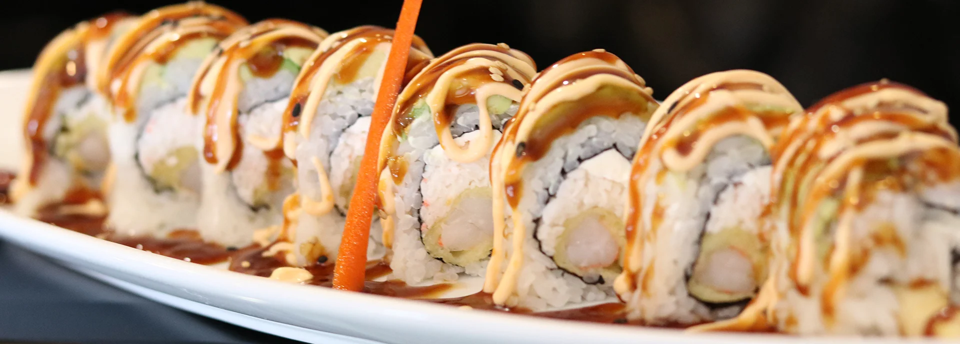 Japanese sushi rolls drizzled with sauce on a white plate