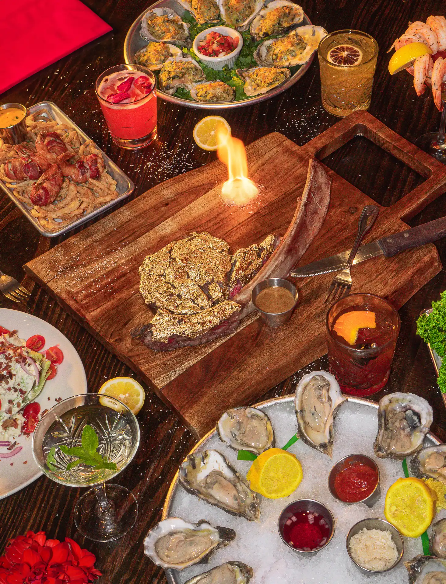 Pour Behavior’s upscale dinner spread featuring a gold-crusted tomahawk steak with live fire, fresh oysters, shrimp cocktail, bacon-wrapped bites, and signature cocktails.