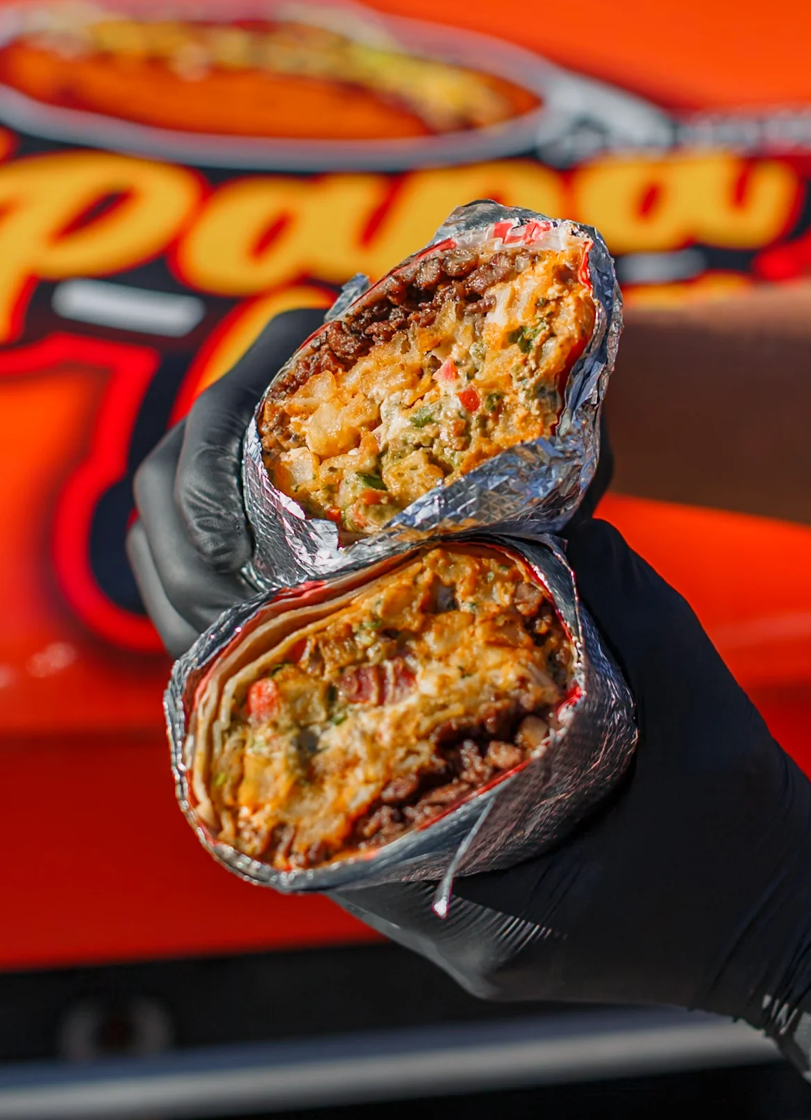 Two halves of a burrito filled with ingredients visible, showcasing a mix of meat and vegetables wrapped in foil.