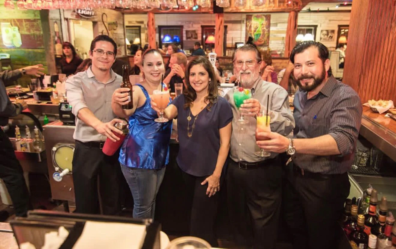 Group of friends toasting with colorful cocktails at a lively bar