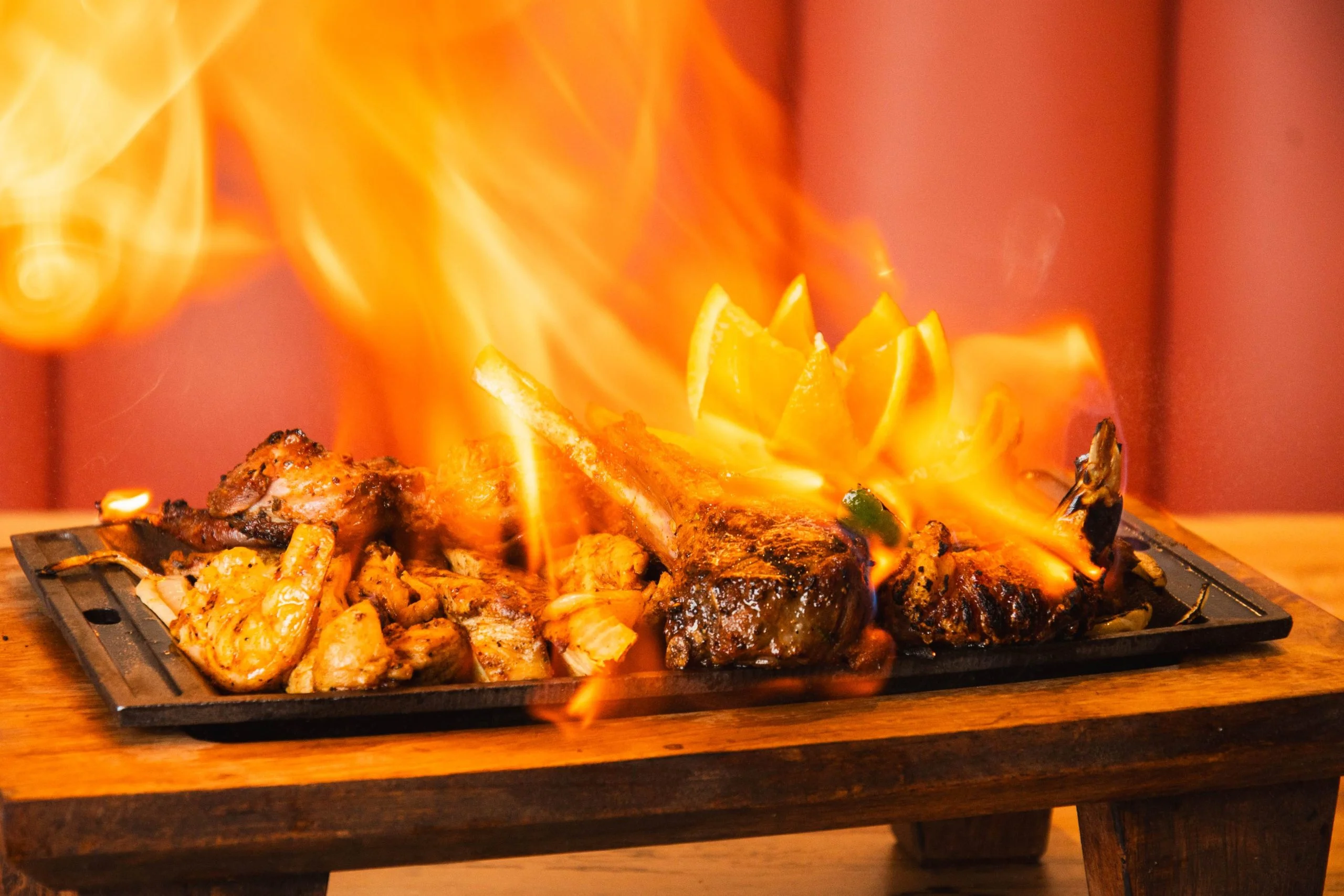 Sizzling mixed grill platter with flames and citrus garnish