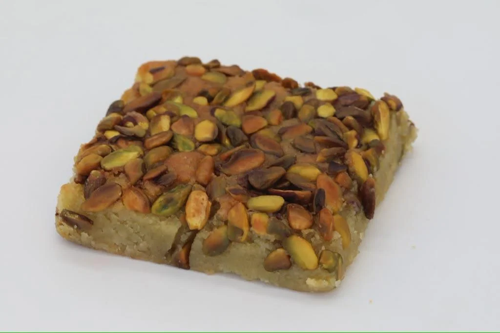 A square piece of sweet confection with a mix of various nuts on top.