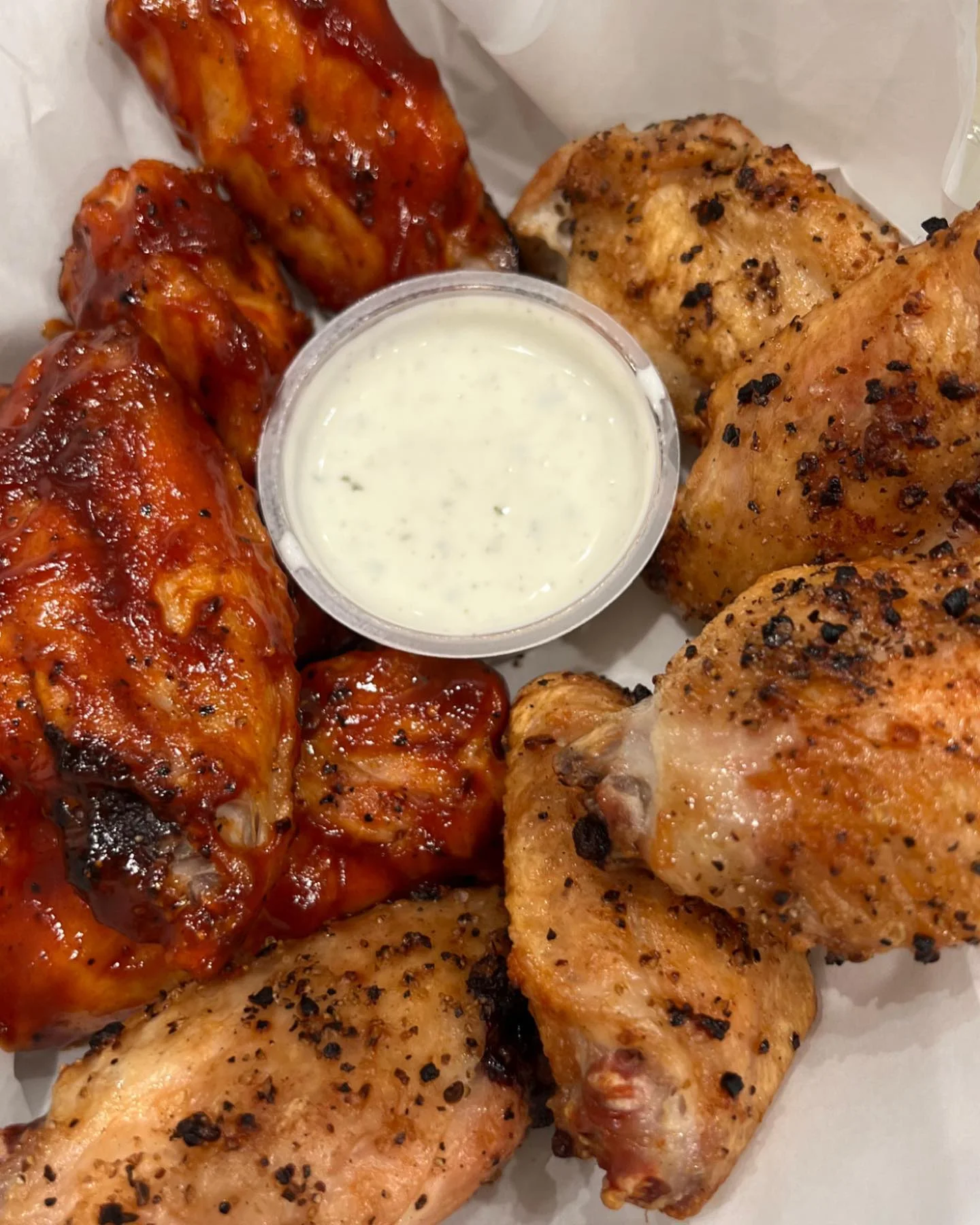 A platter of chicken wings, featuring a mix of barbecue and seasoned wings served with a side of ranch dressing.